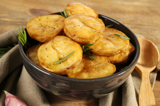 Delicious baked potato with rosemary in bowl on table close up