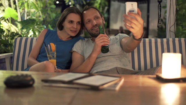 Happy couple raising toast and taking selfie photo with cellphone in cafe 

