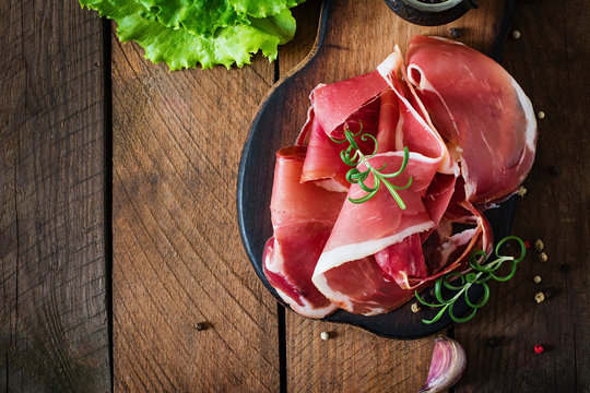 Slices of Prosciutto on old wooden background