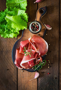 Slices of Prosciutto on old wooden background