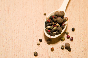 Spoon filled with a mixture of grains of pepper are on a wooden