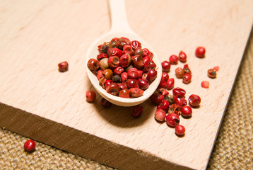 Spoon filled with a mixture of grains of pepper are on a wooden