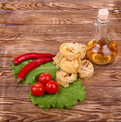 Pasta on the wooden background with tomato, lettuce pepper, olive oil and pepper