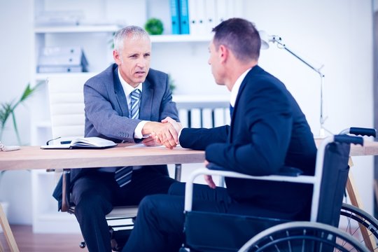 Businessman in wheelchair speaking with colleague 