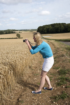 Woman using a digital camera to photograph a field of wheat