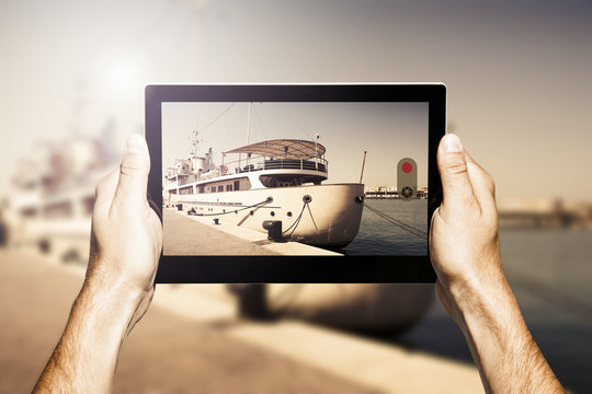 Hands holding a tablet. Taking a photo of luxury yacht docked at port. Vintage filter.