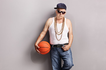 Grumpy senior in a hip-hop outfit holding a basketball - obrazy, fototapety, plakaty