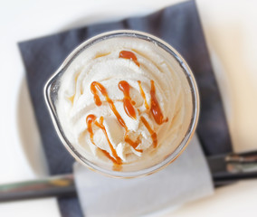 Cup of a fresh caramel latte with whipped cream on table in coff