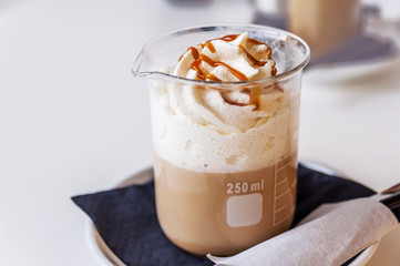 Cup of a fresh caramel latte with whipped cream on table in coff