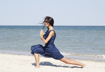 Fototapeta na wymiar Young beautiful woman doing yoga at seaside in blue dress