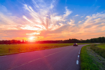 long country road and a beautiful sunset on the background of green field