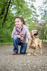 Photo of a little girl kneeling in the park with a dog