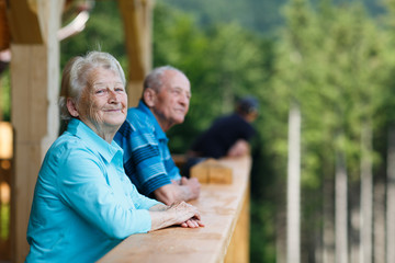Happy senior couple looking to surroundings areas and smiling. Posing in wooden tower and watching for nature scenery in forest. Summer holidays. Blurred forest background. - obrazy, fototapety, plakaty