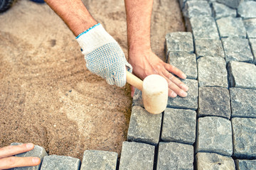 Construction worker installing stone blocks, creating pavement on road, sidewalk or path.
