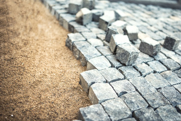 stone pavement, construction worker laying cobblestone rocks on sand