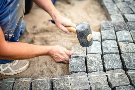 Worker creating pavement using cobblestone blocks and granite stones