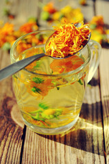 Herbal tea from flowers of a marigold in a transparent glass mug. Medicinal flowers of a calendula.