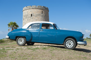 Classic vintage car in ocean blue parked in front of stone tower on a hill in Varadero, Cuba