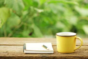 Notebook  and coffee in yellow cup on wooden table