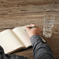 Hand of man writing something in blank notebook