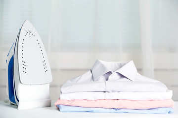 Pile of clothes and electric iron on fabric background