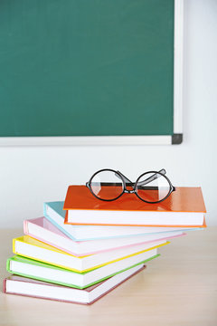 Heap of books and glasses on table in class