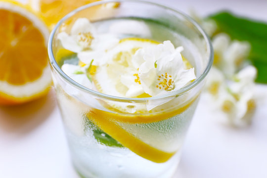Glass of cold refreshing summer drink with flowers and slices of lemon on table close up