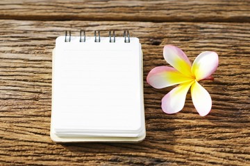 Notebook and plumaria flower on wood table