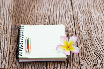 Notebook and pencil with plumaria flower on wood table