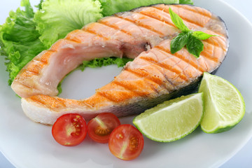 Tasty grilled salmon with tomato and lime on plate close up