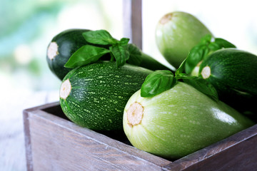 Fresh zucchini with squash and basil in wooden box on bright background