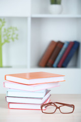 Stack of books with glasses on wooden table in room