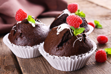 Delicious chocolate cupcakes with berries and fresh mint on wooden table close up