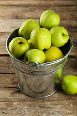 Ripe green apple in metal bucket on wooden table close up