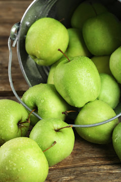 Ripe green apple in metal bucket on wooden table close up