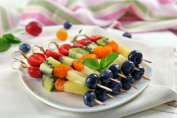 Fresh fruits on skewers in plate on napkin, closeup