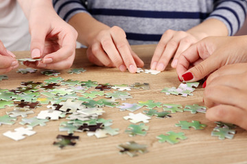 Fototapeta na wymiar Female hands assembling puzzle on wooden table, closeup