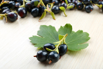 Pile of black currants with green leaves on wooden background
