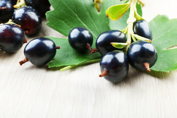 Pile of black currants with green leaves on wooden table, closeup