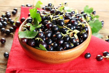 Ripe black currants in bowl on wooden table with red napkin, closeup