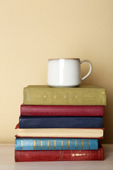 Cup of tea with stack of books on wooden table on light wall background