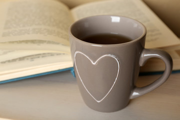 Cup of tea with open book on wooden table, closeup
