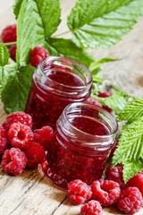 Two jars of raspberry jam, fresh berries and green leaves in an