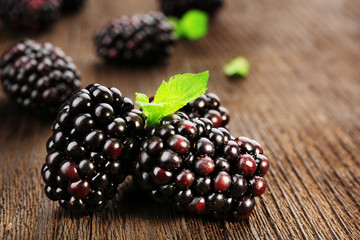 Ripe blackberries with green leaves on wooden table, closeup