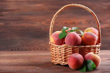 Fresh peaches in wicker basket on wooden background