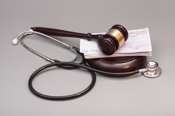 Stethoscope with judge gavel and euro banknotes on gray backgrou