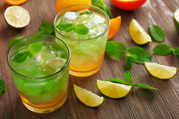Glasses of lime juice with orange on wooden table, closeup