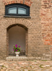 Fototapeta na wymiar Blooming flowers in a vase in the portal brick-stone wall of a m