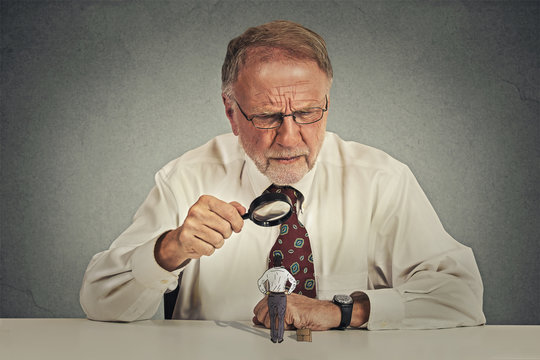 businessman skeptically looking at small employee through magnifying glass