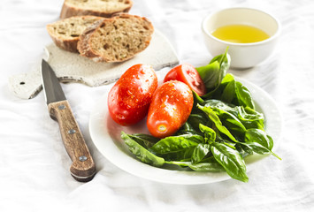 fresh Basil, tomatoes, olive oil and a baguette on a white surface